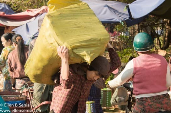 Mandalay, Burma, Myanmar. Zedgyo Market. Boy carries heavy load.